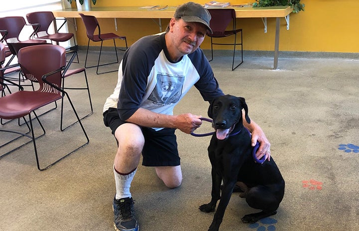 Man posing with a black dog who is sitting next to him