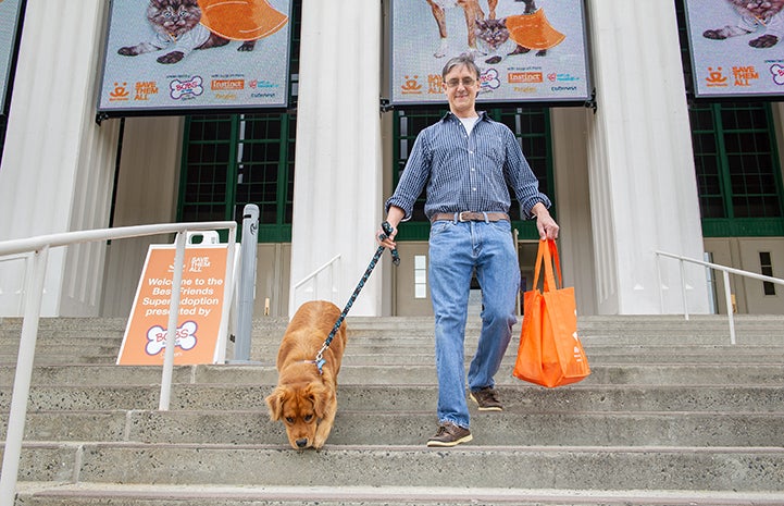 Man walking down the stairs from the New York Super Adoption with a golden retriever he'd just adopted on a leash