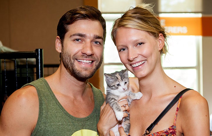 Young man and woman smiling and holding a calico kitten who they adopted at the New York Super Adoption