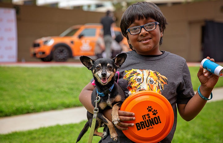 Young boy holding a small black and tan Chihuahua mix and an orange frisbee