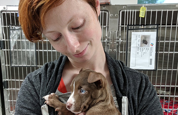Volunteer Jessica Roper snuggling with a puppy in front of some kennels