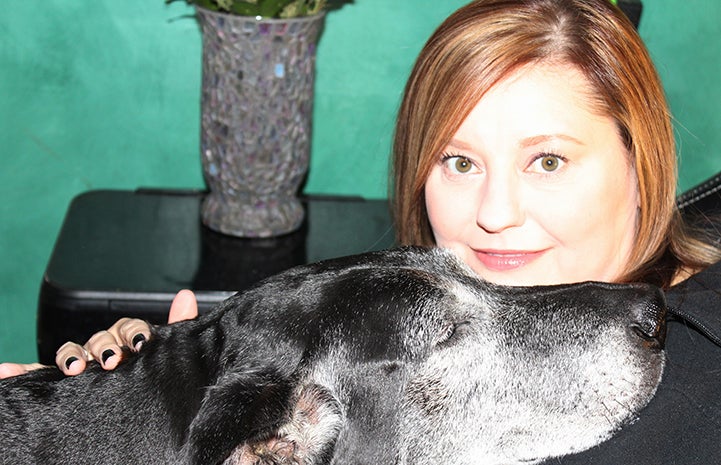 Volunteer Laura Rozler posing with a black dog with a graying muzzle
