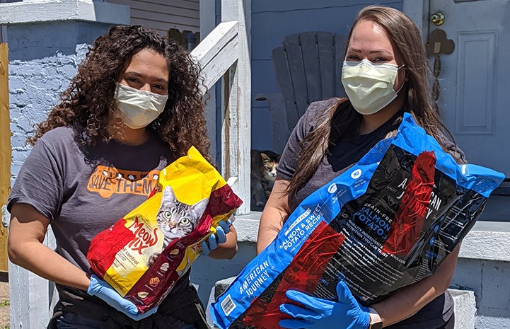 Two gloved and masked women holding large bags of pet food