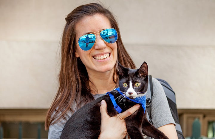 Woman wearing sunglasses holding Candycane the kitten, who is wearing a blue harness