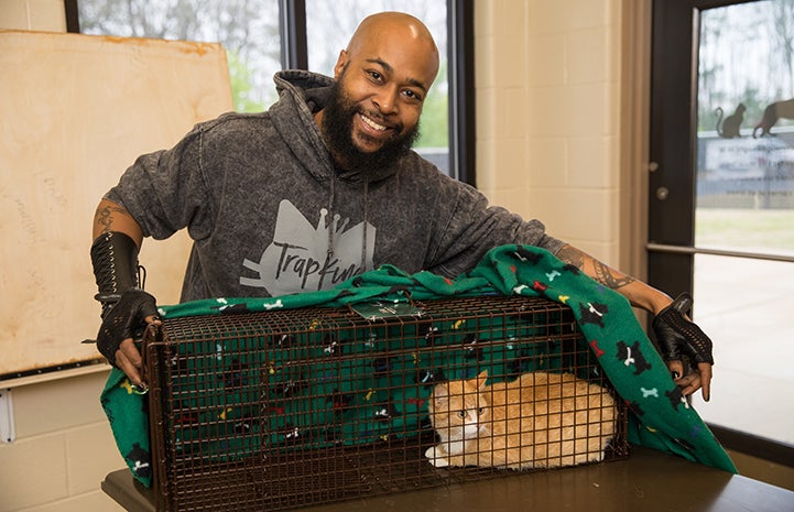 Sterling “Trap King” Davis holding a live trap holding an orange and white cat