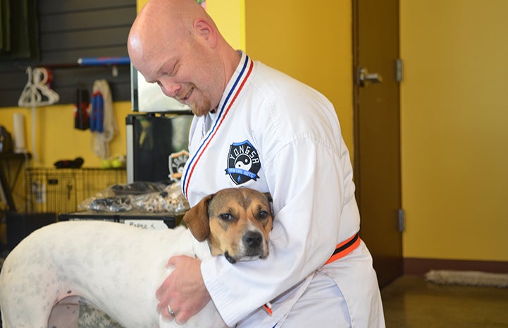 Man wearing a taekwondo outfit giving a hug to Alice the dog