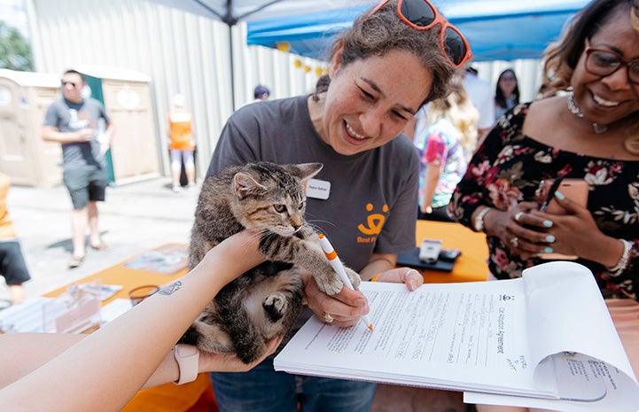 Volunteer Deyra Galvan smiling and helping complete some paperwork for a calico cat