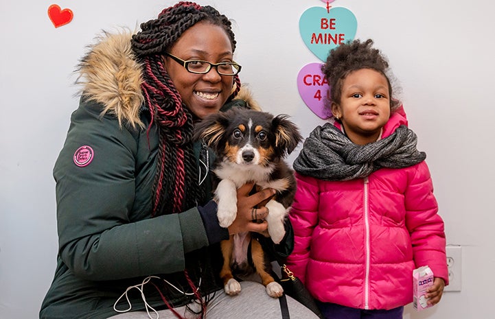 Woman and child who adopted a small fluffy dog, standing in front of Valentine's Day hearts at the adoption event