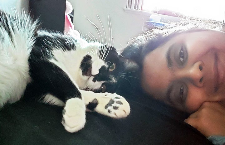 Smiling Ana Merkulova lying head-to-head next to black and white cat