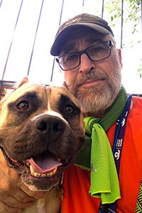 Volunteer David Glazer wearing a green scarf and taking a selfie with a big brown dog