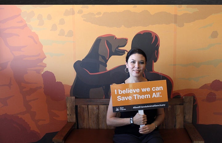 Volunteer Chelsea Eng at the Best Friends Visitor's Center holding a sign that says, I believe we can Save Them All