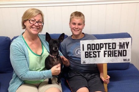 Lillie Schlessinger and her son after adopting Chispa the dog, holding a sign that says, I adopted my best friend