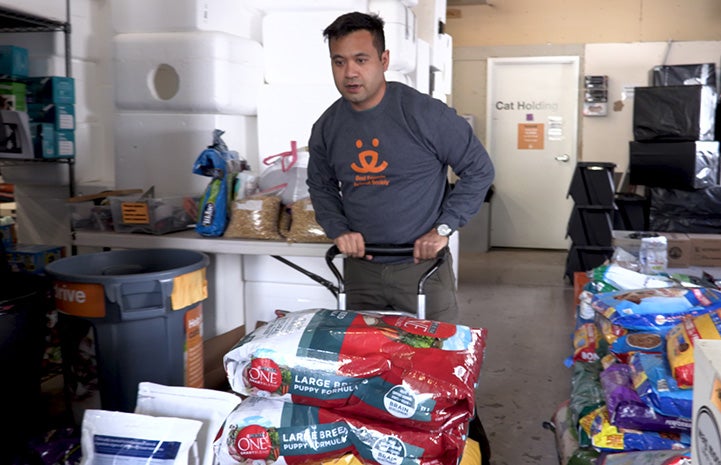 Volunteer Christian Ordonez moving large bags of dog food on a cart