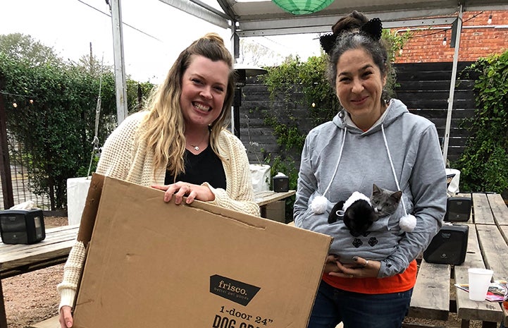 Volunteer Deyra Galvan wearing cat ears with another woman holding a box and a litter of kittens