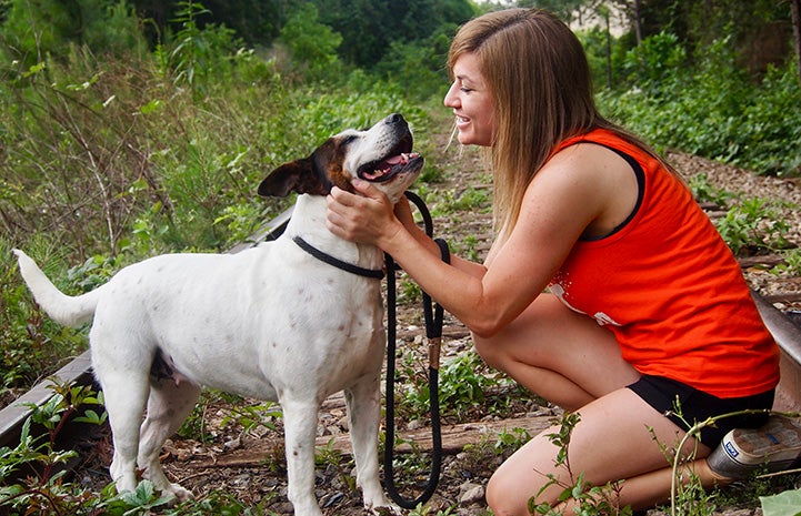 Volunteer Jamie Serratell squatting down and petting a white and brown dog in some unused railroad tracks