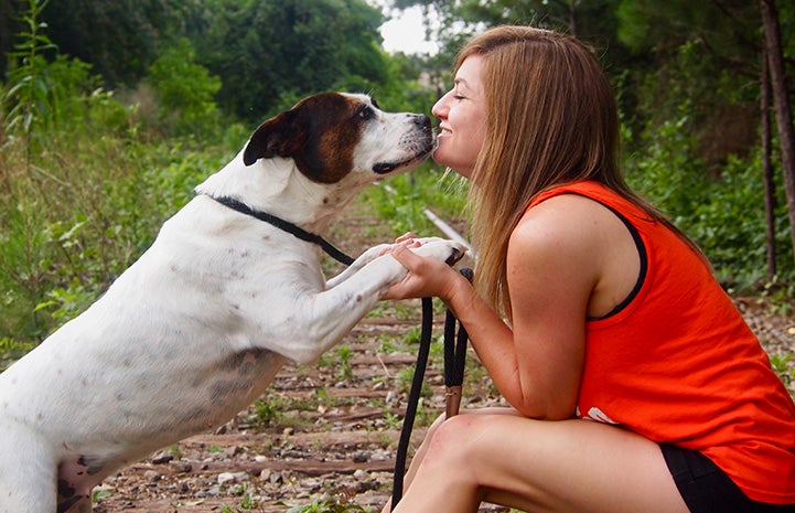 Volunteer Jamie Serratell holding the paws and looking face-to-face with a white and brown dog
