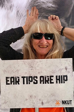 Volunteer Judy Steiger holding an Ear Tips Are Hip sign while positioning her hands above her head like cat ears
