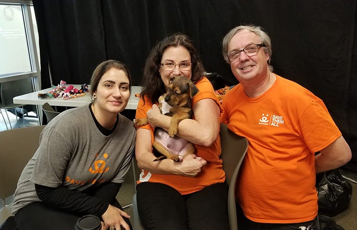 Volunteer Kristin Biggs holding a small brown puppy with two other volunteers sitting next to her