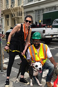 Volunteer Lauren Fishman walking a black and white dog while standing next to a man wearing a hard hat and bright yellow safety vest