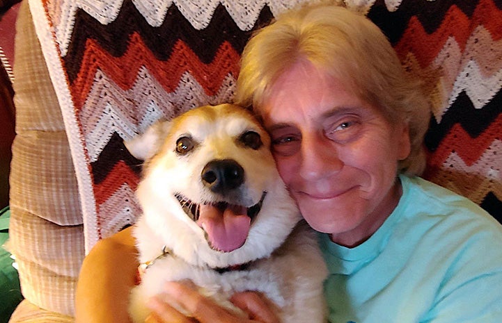 Volunteer Kathy Posekel hugging a tan and white dog with an afghan blanket behind them