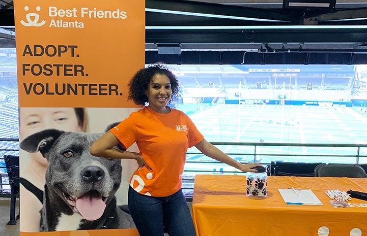 Volunteer Nisha Gross wearing an orange Best Friends T-shirt and standing at a Best Friends booth