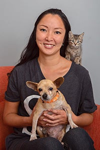 Volunteer Ranko Fukuda with a tan Chihuahua on her lap and a kitten on her shoulder