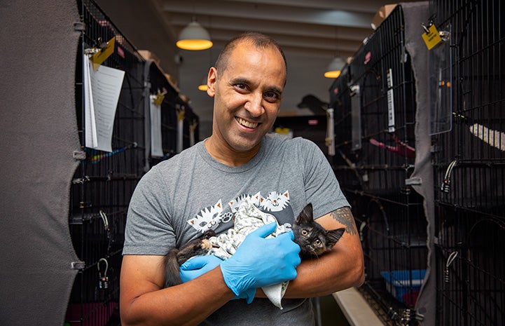 Volunteer Robert Lobo cradling a kitten in his arms standing in front of kennels