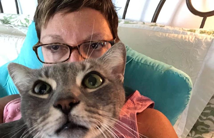Volunteer Tracey Paige posing in a selfie with a gray tabby cat in front of her