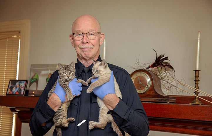 Michael Moran holding two foster kittens, while standing in front of a mantle