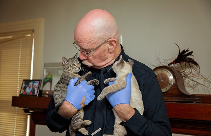 Volunteer Michael Moran holding two foster kittens while looking down at one of them