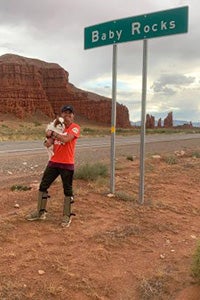 Becky McCrea holding her dog Arnie in front of a Baby Rocks road sign with cliffs in the background
