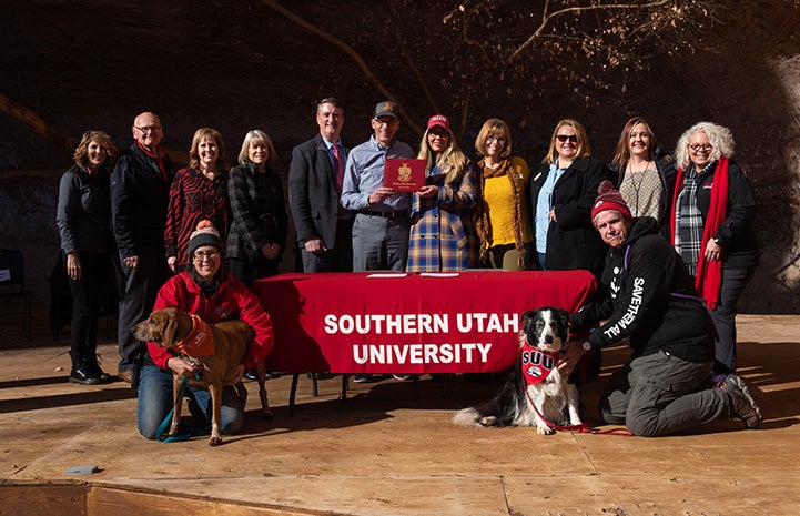 Group of people and a dog posing with a Southern Utah University banner 