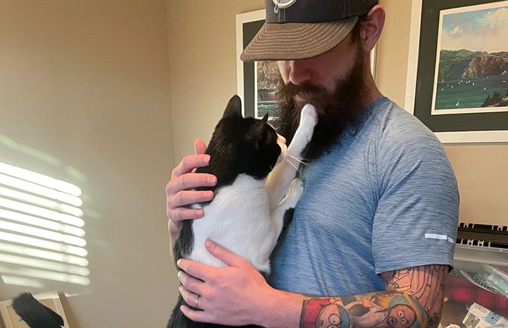 Nino the cat reaching his paw up to his person Max to touch his beard