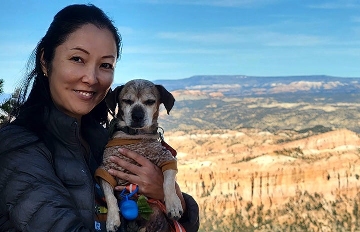 Ranko holding Soba the dog in front of red rock formations behind them