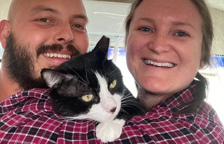 Smiling couple holding Monroe the black and white cat