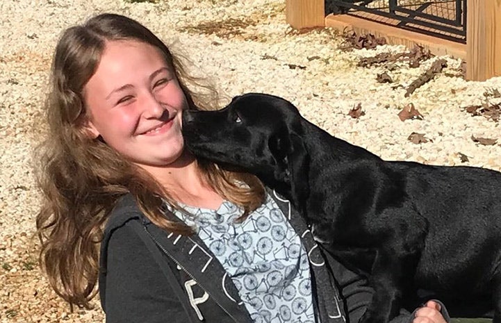 Smiling person with a black puppy looking at her face