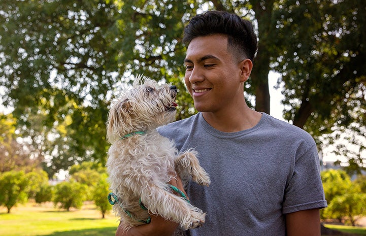 Smiling man holding a small fluffy tan dog outside