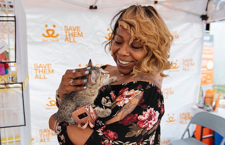 Smiling woman holding a tabby kitten with a Best Friends backdrop behind them