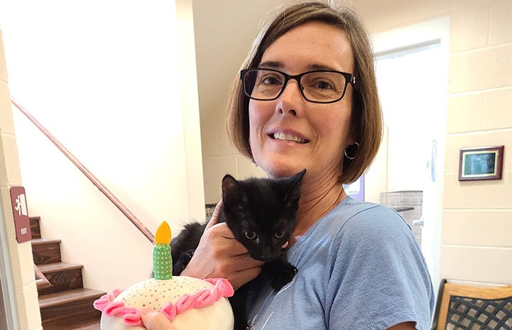 Woman holding a black cat and the stuffed cake with candle