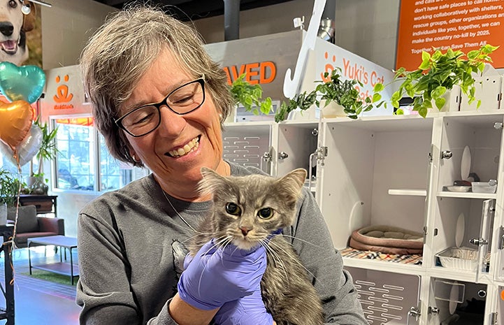 Volunteer Tana Hunter smiling and holding a gray tabby cat