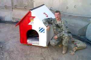  US soldier Peter kneeling next to a dog house 