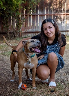 Young girl with dark hair sitting next to brown dog
