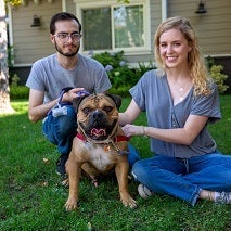 Couple sitting in grass with brown and white dog 