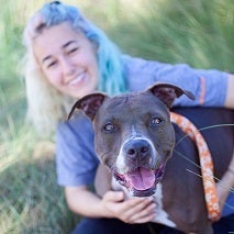 Woman with blue hair in gray shirt sitting with gray and white dog