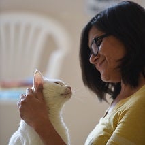 Woman with dark hair wearing yellow shirt petting white cat