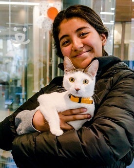 Young woman with long dark hair wearing dark coat holding cat