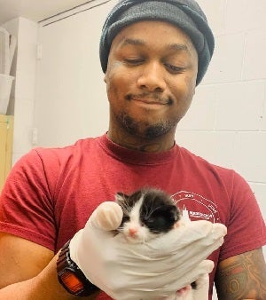 Man wearing stocking cap and red shirt holding black and white kitten