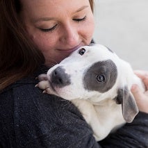Woman in black jacket holding white dog with gray spot over eye