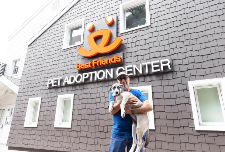 Smiling person holding a dog outside of the Best Friends Pet Adoption Center in Los Angeles