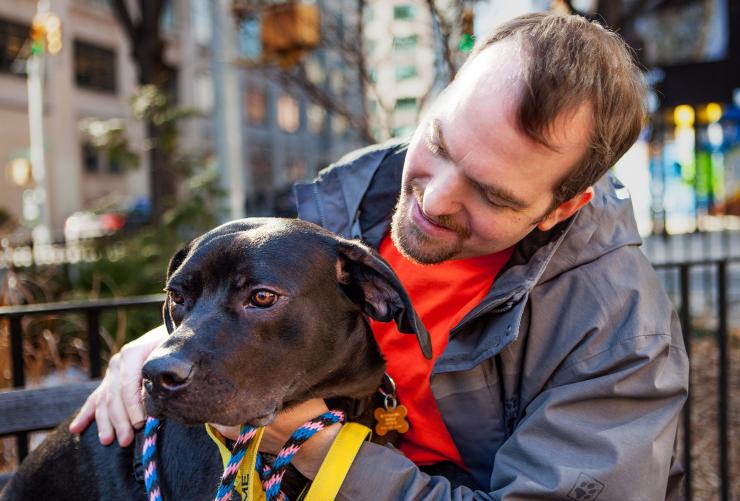 Smiling person sitting in a park in New York City with a dog